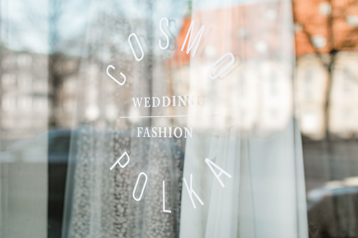 Das Logo von Cosmopolka wedding | fashion auf der Schaufensterscheibe des Ladens.