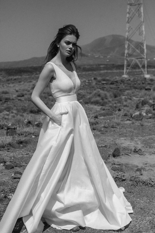Ein Model steht in einem weißen, langen Hochzeitskleid aus Seide in einer weiten Landschaft