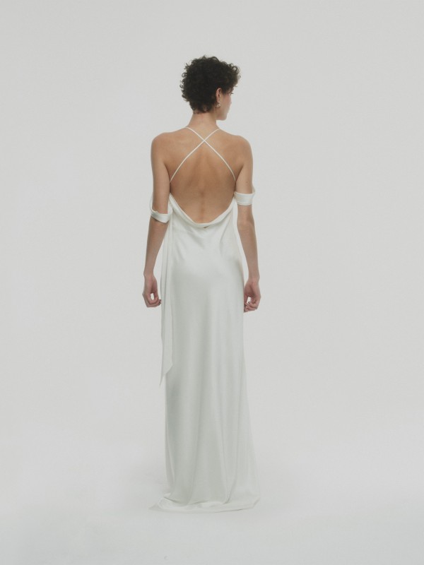 Rückenfreies Brautkleid mit eleganten schmalen Trägern und fließendem weißen Stoff, Braut von hinten vor hellem Hintergrund