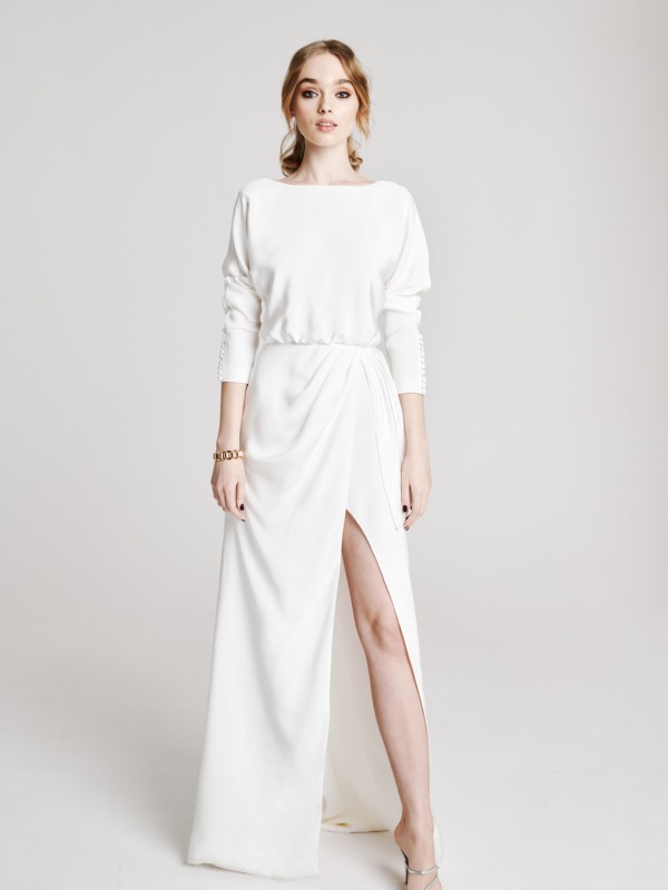 Clean-Brautkleid mit drapiertem Rock, langen Ärmeln und hohem Beinschlitz, modernes und schlichtes Design, Braut mit blonden Haaren und Armband vor hellem Hintergrund