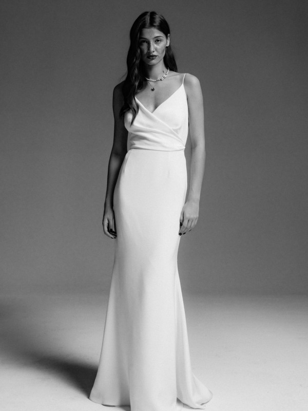 Schlichtes Clean-Brautkleid mit schmalen Spaghettiträgern und Wickeloptik am Oberteil, glatter Stoff, Braut mit offenem dunklem Haar im Schwarzweiß-Look vor neutralem Hintergrund