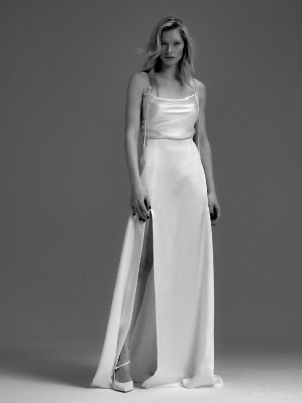 Schlichtes Clean-Brautkleid mit schmalen Spaghettiträgern, glattem Stoff und hohem Beinschlitz, Braut mit offenem blondem Haar im Schwarzweiß-Look vor neutralem Hintergrund