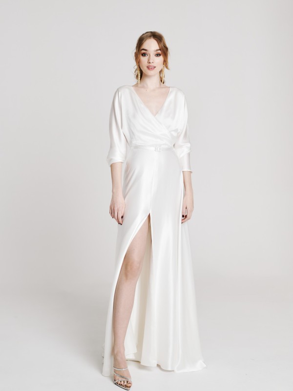Brautkleid mit langem Ärmel aus fließendem Satin mit Wickeloberteil, hohem Schlitz und schlichten Riemchensandalen in einem hellen Studio