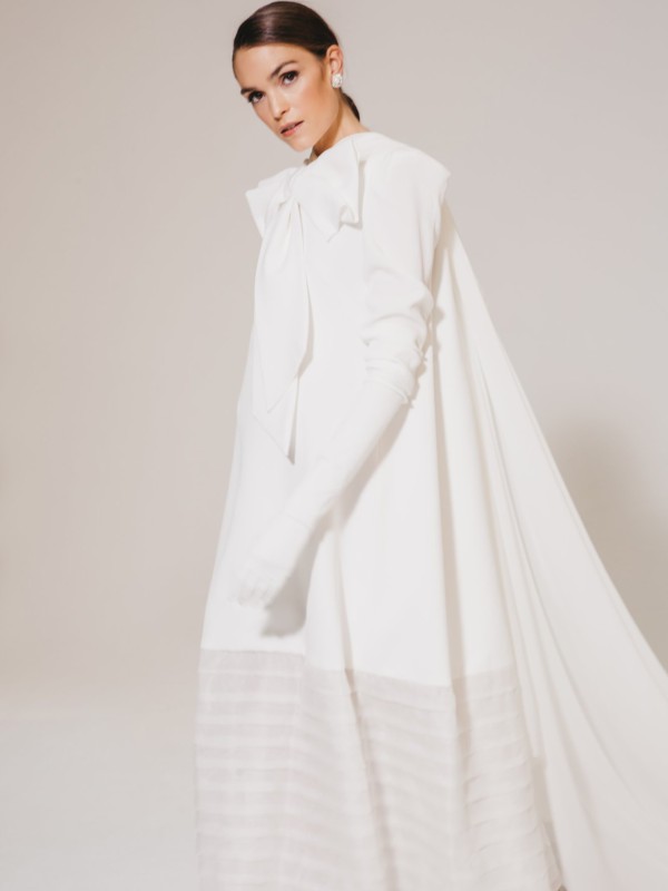 Modernes Brautkleid mit langen Ärmeln und großer Schleife am Ausschnitt.