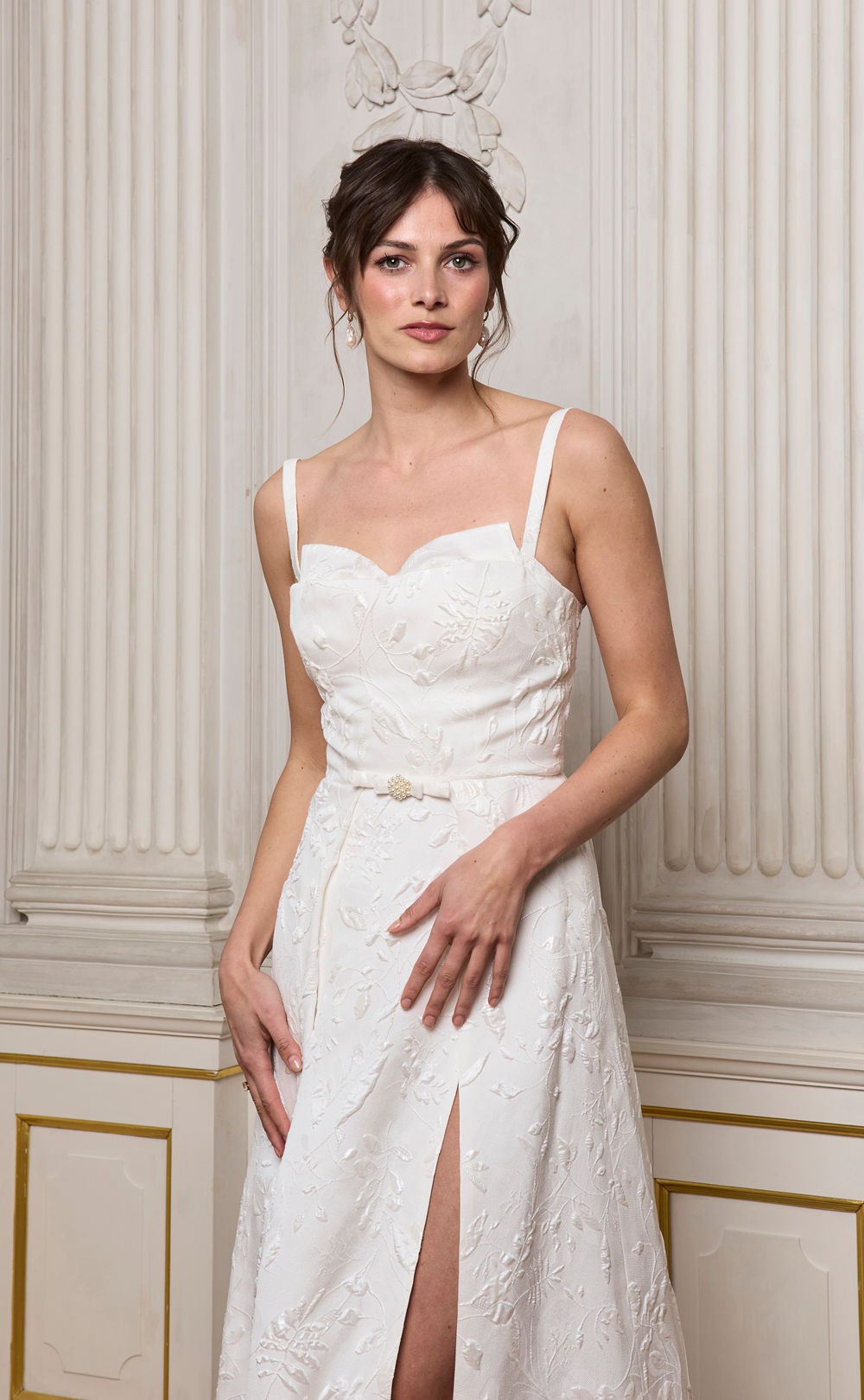 Model in einem klassischen, langen Brautkleid steht vor einer reich verzierten Wand