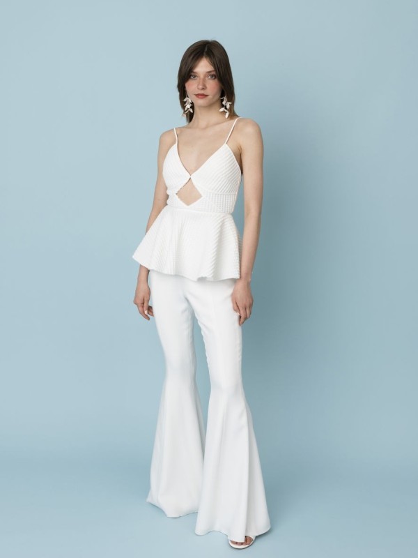 Braut trägt figurbetontes Spaghettiträgertop mit Schößchen und ausgestellte Schlaghose vor hellblauem Hintergrund