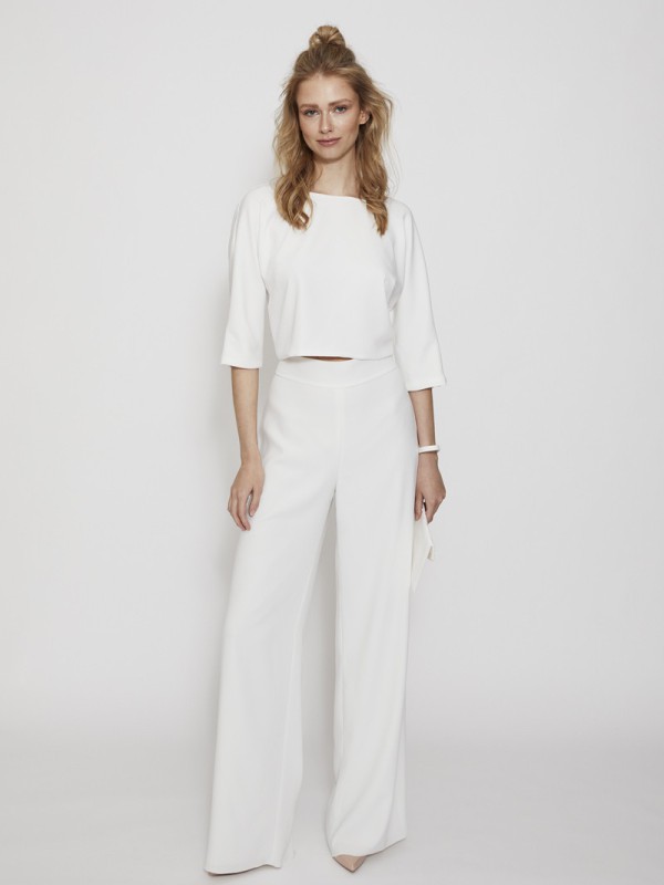 Braut trägt minimalistisches weißes Hochzeitsoutfit mit 3/4-Arm-Top und weiter Hose