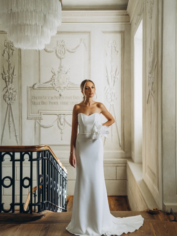 Klassisches trägerloses Brautkleid mit schmaler Silhouette und großer Blütenapplikation an der Taille in einem historischen Saal