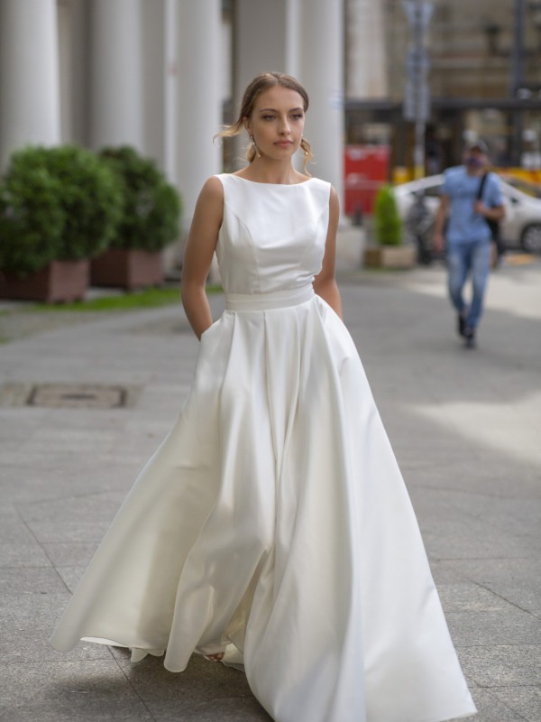 Klassisches Brautkleid mit hohem Rundhalsausschnitt betonter Taille und weit schwingendem Rock mit Taschen in der Stadt