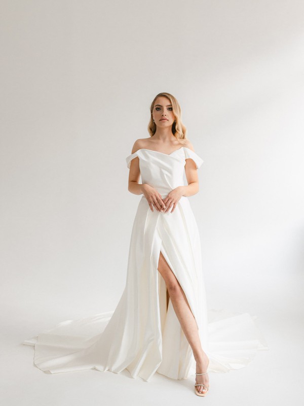 Klassisches Brautkleid mit schulterfreiem Ausschnitt hohem Schlitz und fließender Schleppe im hellen Studio