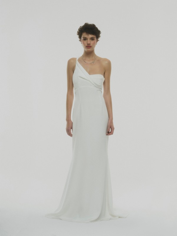 Ein Model vor einem weißen Hintergrund trägt ein elegantes One Shoulder Brautkleid aus leichter Seide mit einem schmalen Träger.