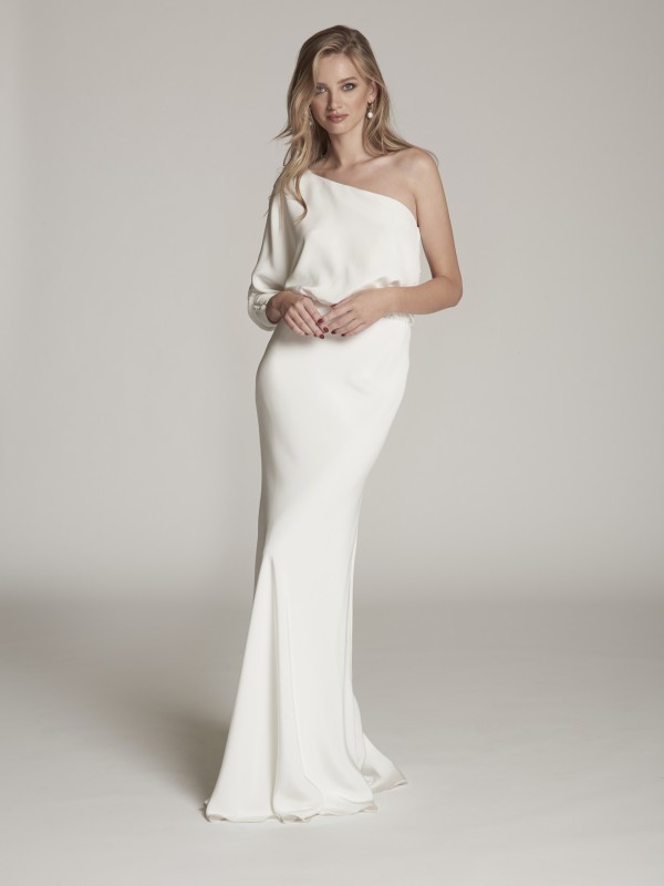 Model in einem engen Mermaid-Brautkleid mit einer Schulter vor weißem Hintergrund.