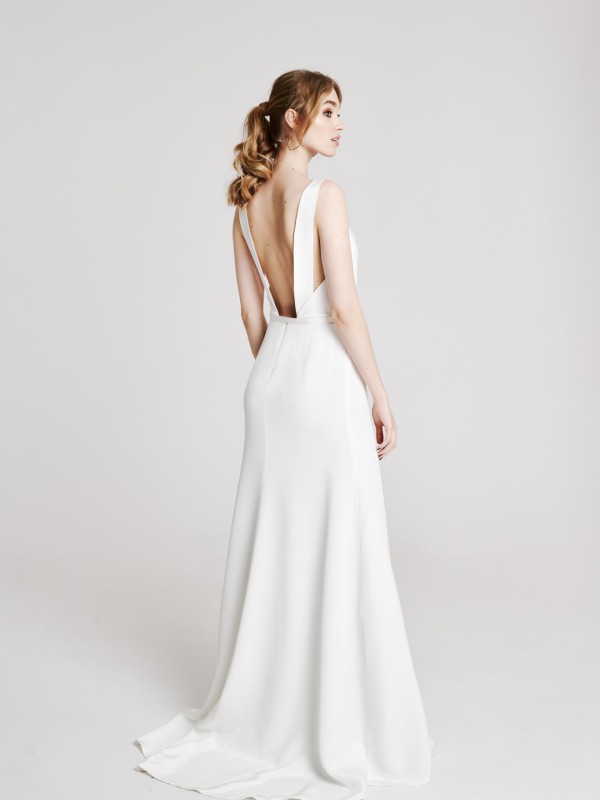 Weißes rückenfreies Brautkleid mit breiten Trägern und tiefer Rückenpartie, schwingender Rock, Braut im romantischen Look vor hellem Hintergrund