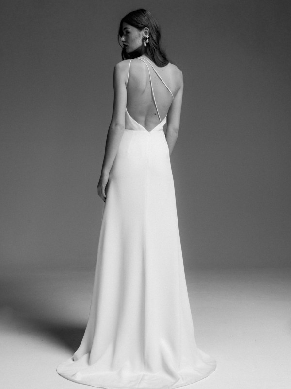 Minimalistisches rückenfreies Brautkleid mit überkreuzten Spaghettiträgern, fließende Silhouette und moderne Eleganz, Braut mit offenem Haar und auffälligem Ohrschmuck im Schwarzweiß-Look vor dunklem Hintergrund