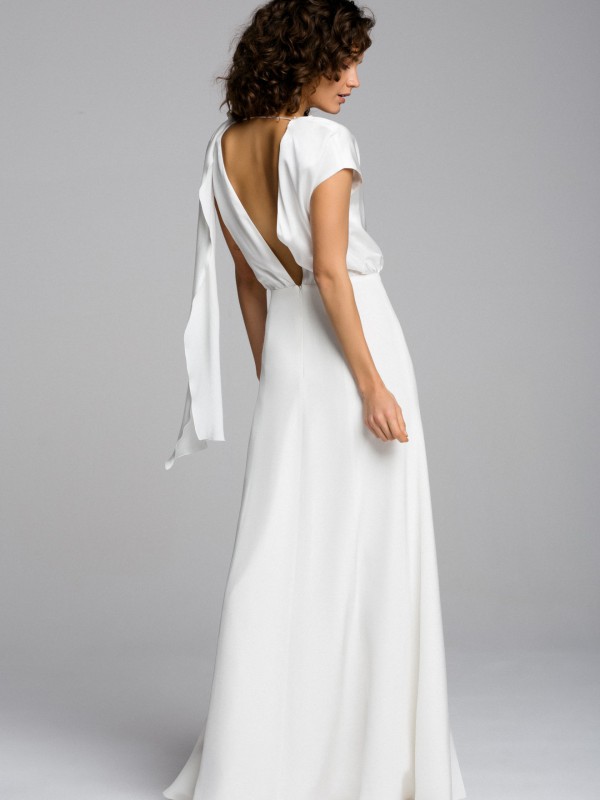 Modernes rückenfreies Brautkleid mit drapierter Schulter und langem Stoffband, eleganter fließender Rock, Braut mit lockigem Haar vor hellem Studiohintergrund