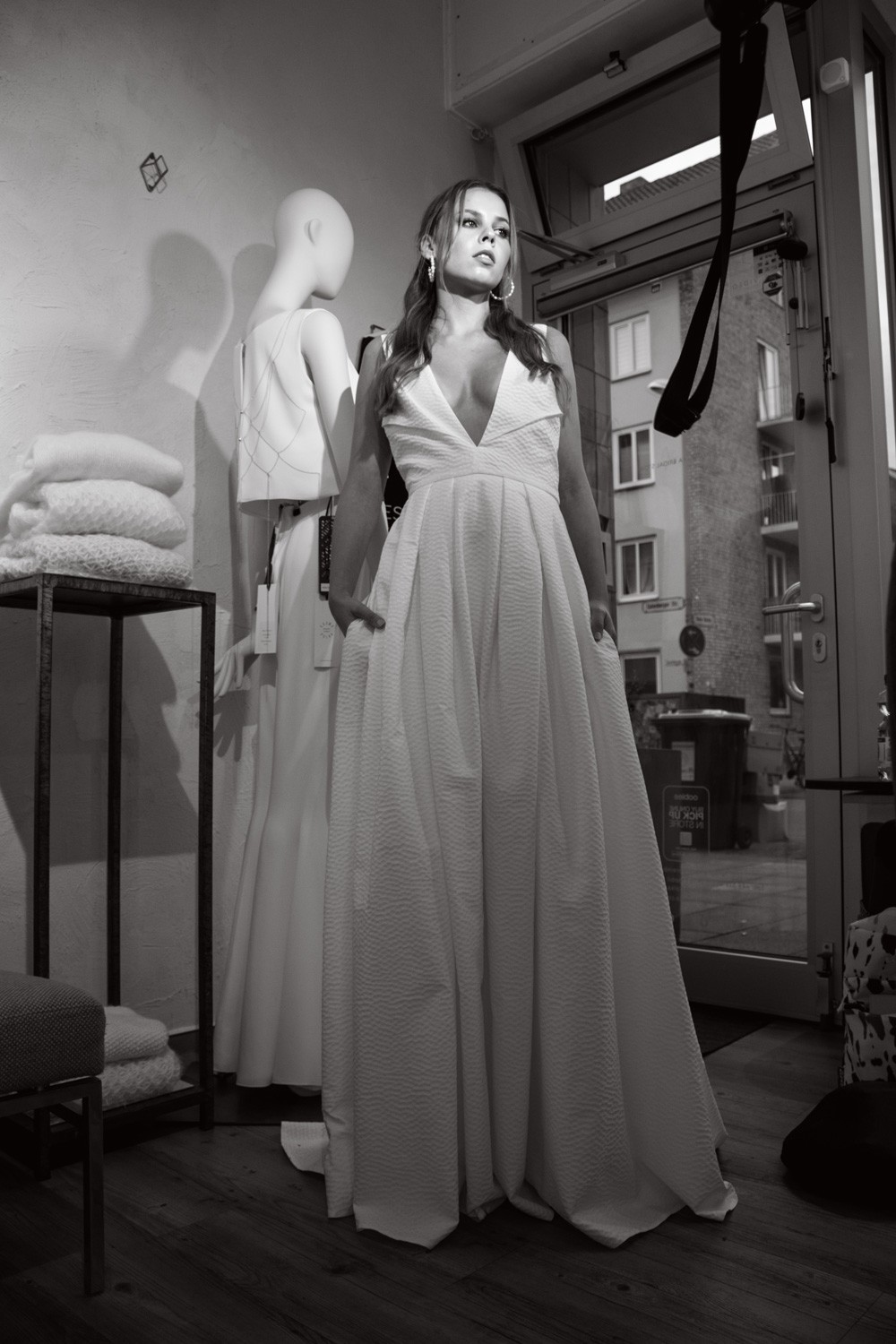 Braut im weißen Kleid steht im COSMOPOLKA Bridal Store Hannover neben einer Schaufensterpuppe.