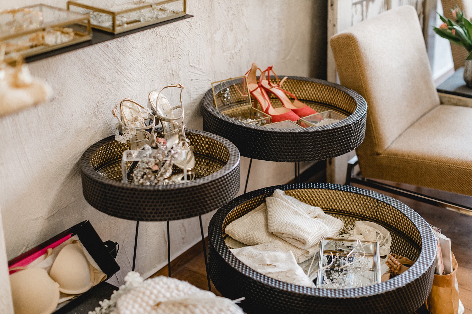 Detailaufnahme aus dem COSMOPOLKA Bridal Store Hannover: runde Körbe mit Brautschuhen, Schmuck und Accessoires neben einem beigen Sessel und Holzboden.