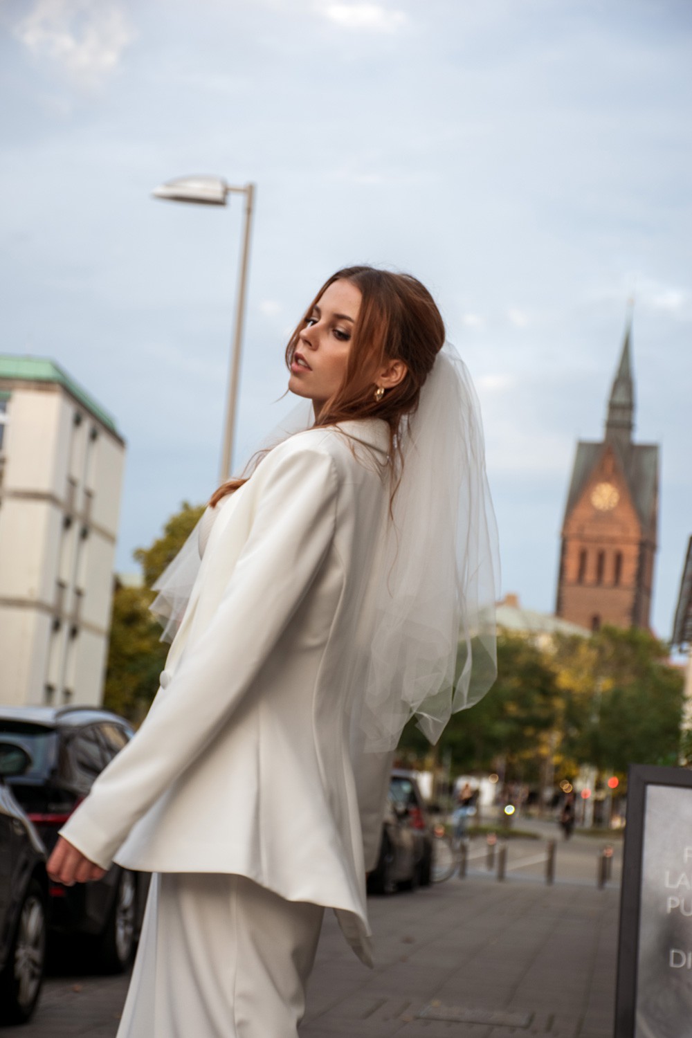Braut mit weißem Blazer und Schleier vor der Marktkirche in Hannover, modern gestylt auf einer Hannoveraner Straße.