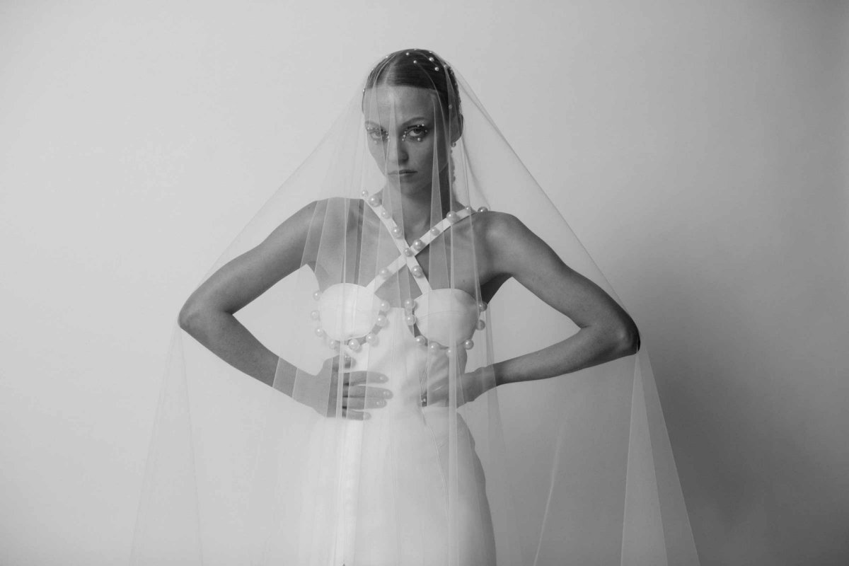 Eine Frau posiert in einem weißen Brautkleid und langem Schleier vor der Kamera.
