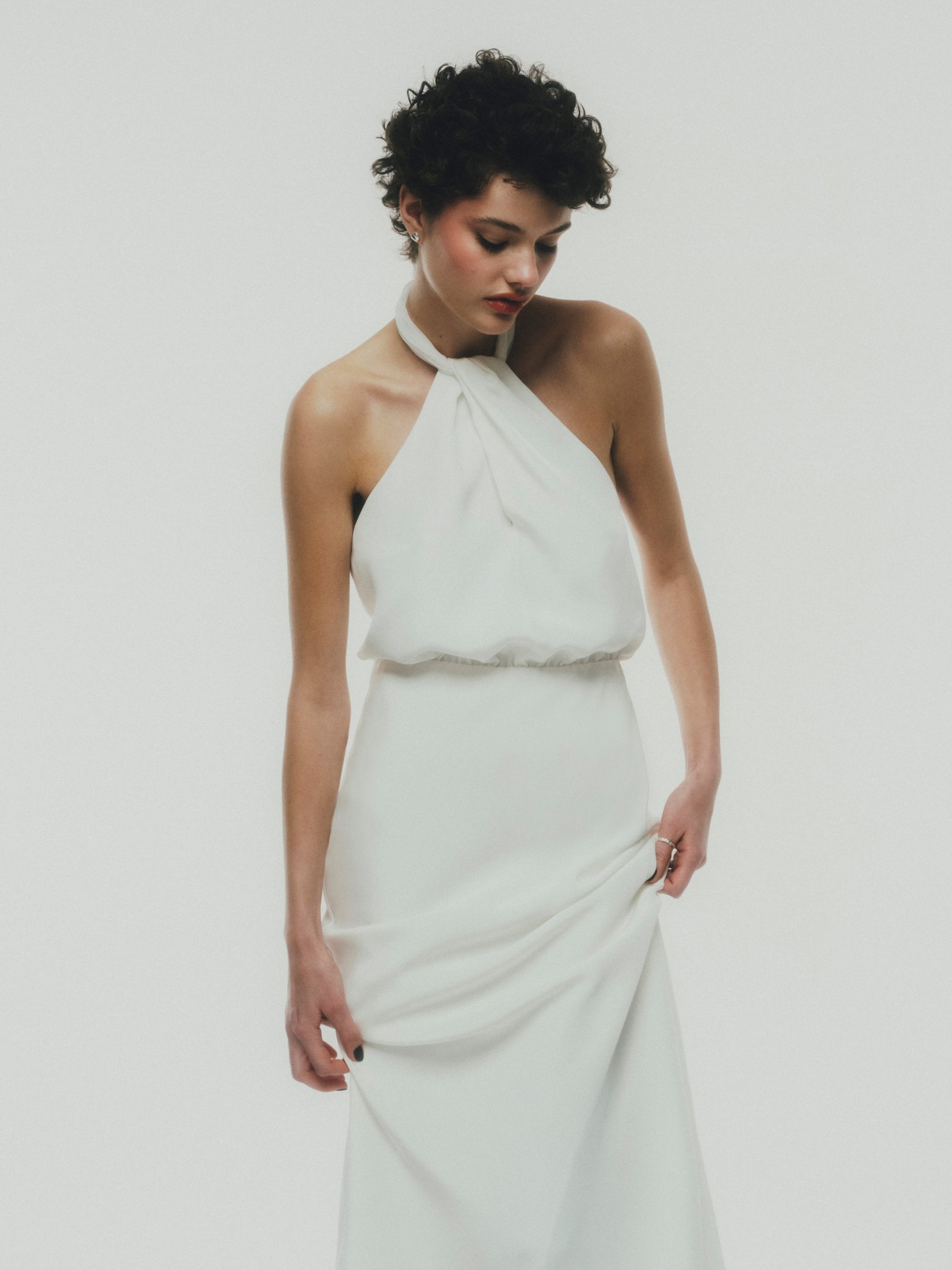 Model in schlichtem Designer-Brautkleid mit Neckholder vor hellem, minimalistischem Hintergrund