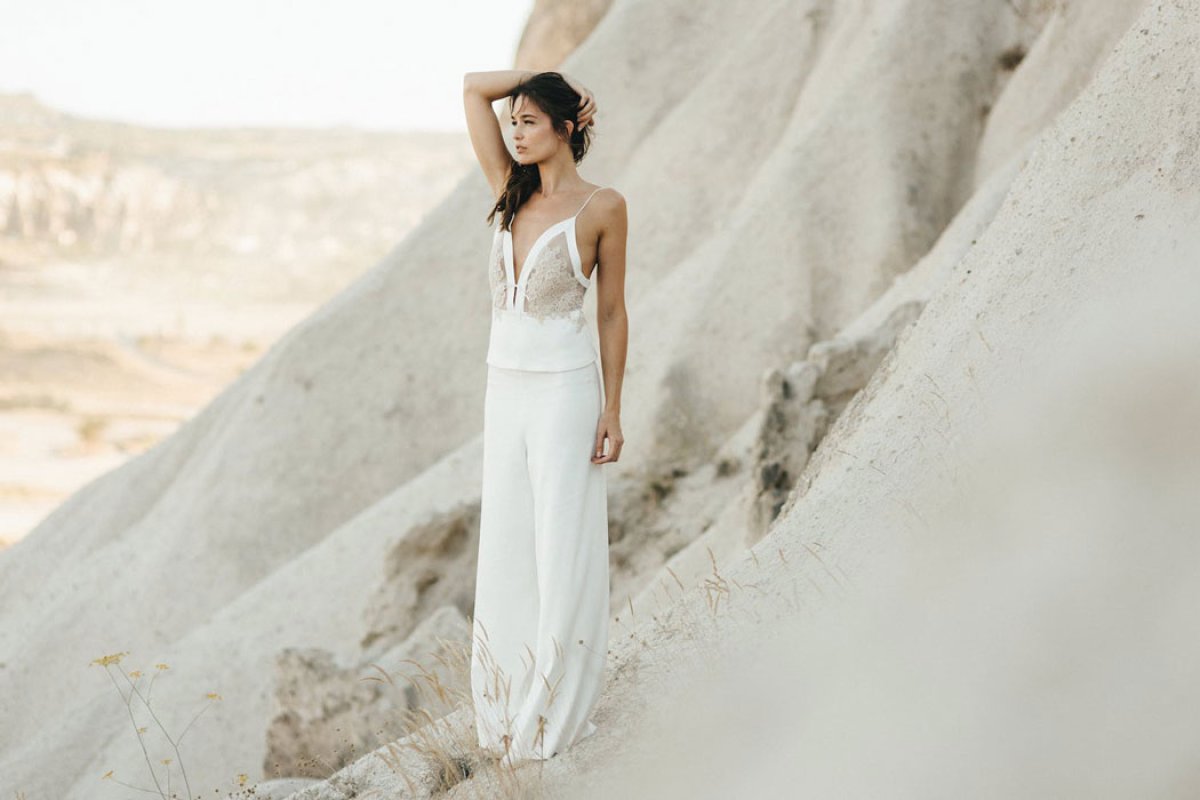 Ein Model posiert in einem weißen Top und einer weißen Hose am Rande eines Felsens in der Wüste.