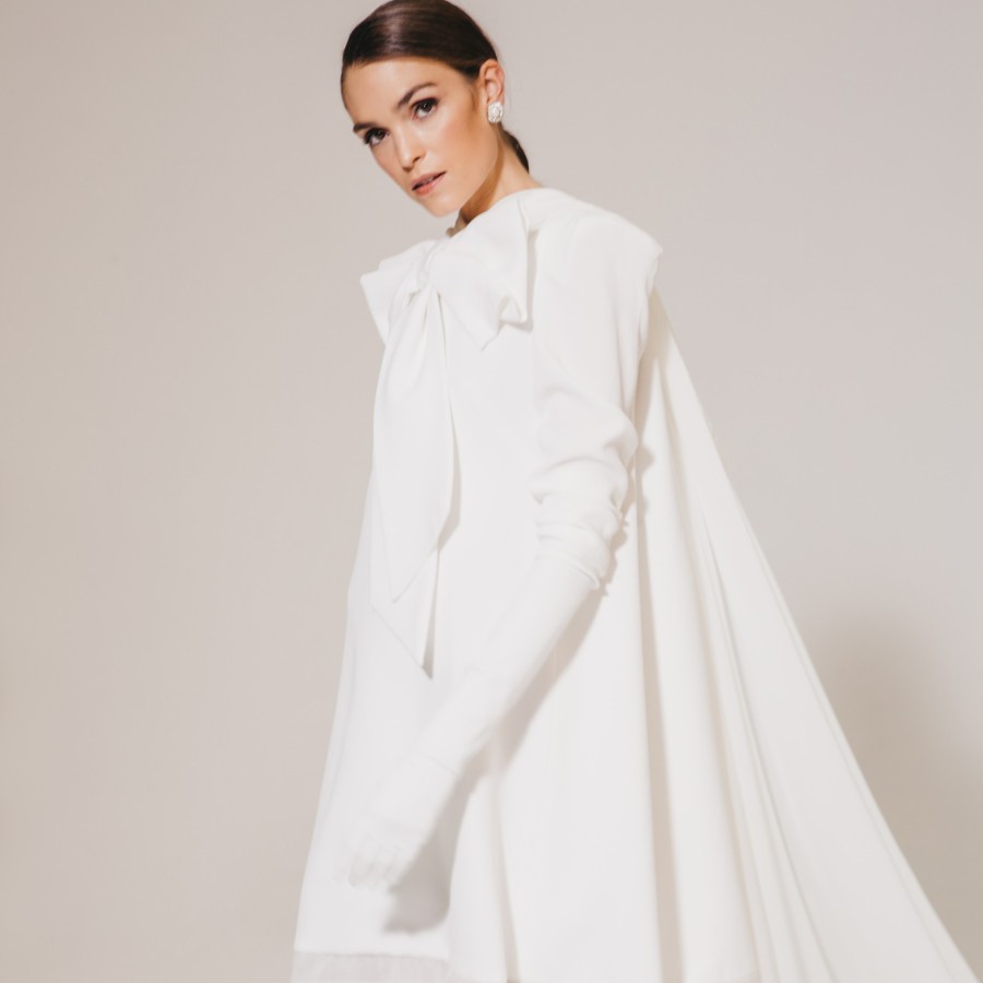 Braut in einem modernen Brautkleid aus Seide und mit großer Schleife, posiert in einem Atelier vor hellem Hintergrund.