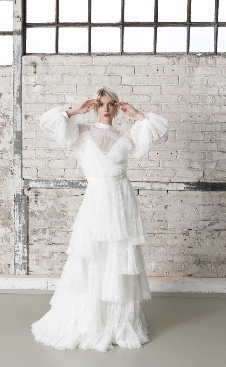 Eine Braut im langen Brautkleid mit Rüschen steht in einer leeren Fabrikhalle.