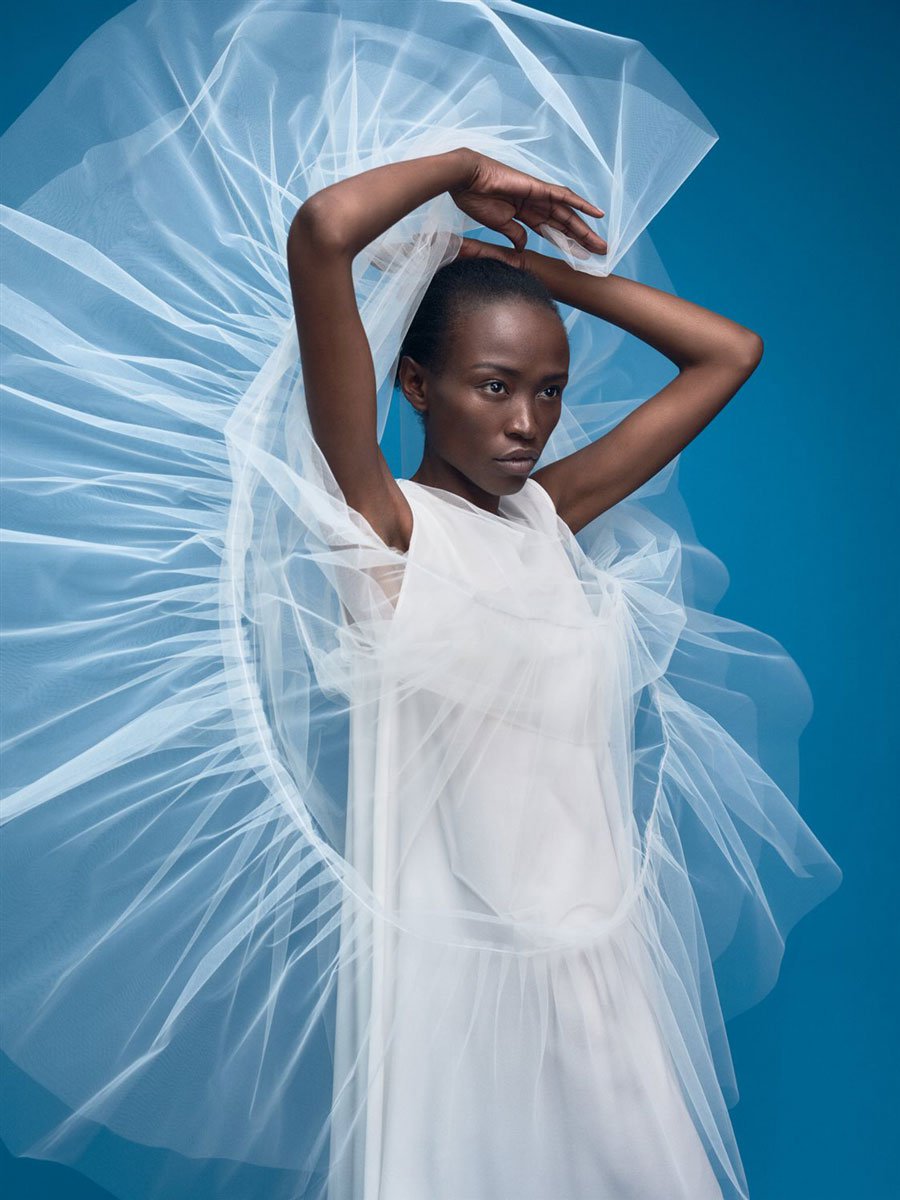 Ein Model posiert im weißen Brautkleid vor einem blauen Hintergrund.