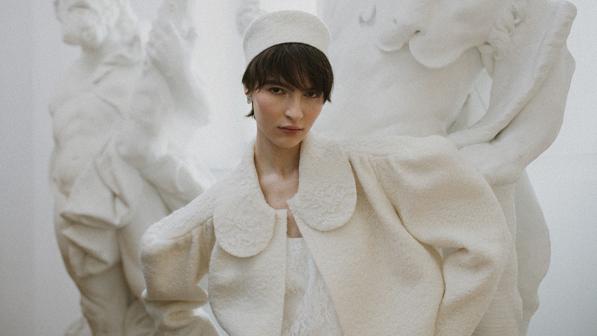 Eine Braut in einem strukturiertem, weißem Hochzeitscape und einer Kopfbedeckung posiert vor der Kamera.