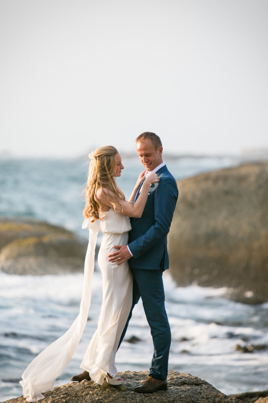 Brautpaar steht auf einem Stein und befestigt Blume am Anzug