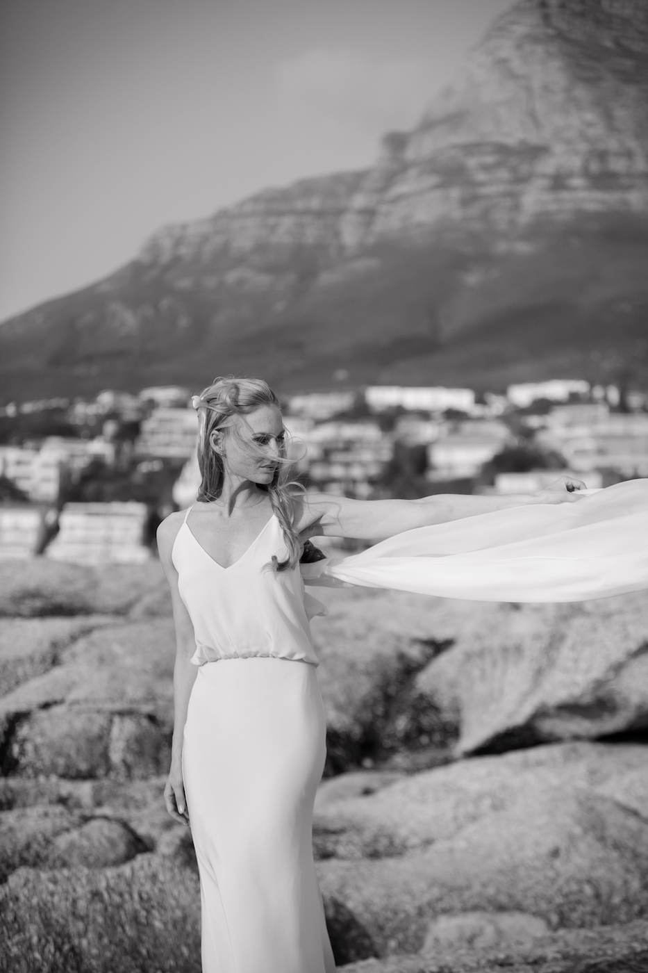 Braut in einem eleganten, schlichten Brautkleid vor einer Berglandschaft schwarz weiß fotografiert.