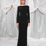 Auf dem Foto ist ein elegantes, schwarzes Maxikleid zu sehen, das durch seine schlichte, figurnahe Silhouette und den verführerischen Rückenausschnitt besticht. Das Kleid hat lange, schmale Ärmel und einen hochgeschlossenen Ausschnitt vorne, was ihm eine zeitlose, klassische Eleganz verleiht. Der Rückenausschnitt setzt einen sinnlichen Akzent und macht das Design besonders spannend. Der Stoff fällt glatt und fließend bis zum Boden, wodurch die Figur der Trägerin stilvoll umschmeichelt wird. Der Hintergrund ist mit drapierten, hellen Stoffbahnen gestaltet, die das schwarze Kleid hervorheben und dem Bild eine edle, luxuriöse Atmosphäre verleihen. thumbnail