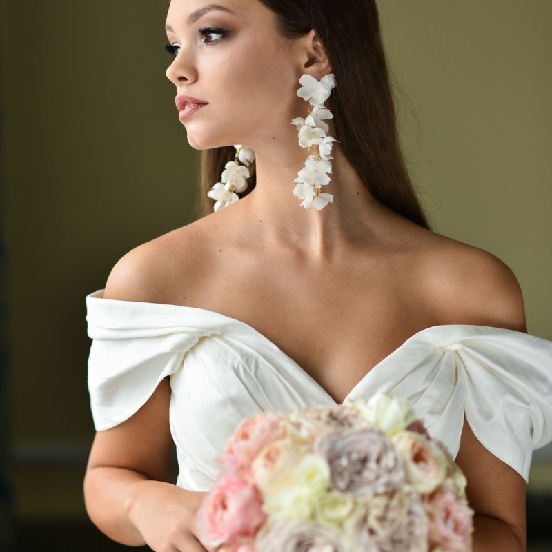 Model mit Ohrringen 'Bloom', verziert mit weißen Seidenblüten und goldenen Akzenten, Seitenansicht, eleganter Brautschmuck.