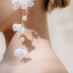 Nahaufnahme eines Models mit 'Mollis'-Ohrringen, verziert mit weißen Seidenblüten und Perlen, eleganter Brautschmuck. thumbnail