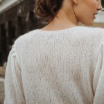 Detailaufnahme der Rückansicht eines zarten Braut-Cardigans aus Cashmere. Der Fokus liegt auf dem Strickmuster, das die feine Handarbeit des Kleidungsstücks hervorhebt. Eine Perlenhaarband ergänzt den eleganten Look. thumbnail