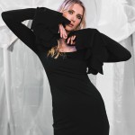 Model in schwarzem Midikleid mit weiten Ärmeln, posiert mit erhobenen Armen vor einem drapierten Hintergrund. Das Kleid betont eine elegante, figurbetonte Silhouette und künstlerische Ausstrahlung. thumbnail