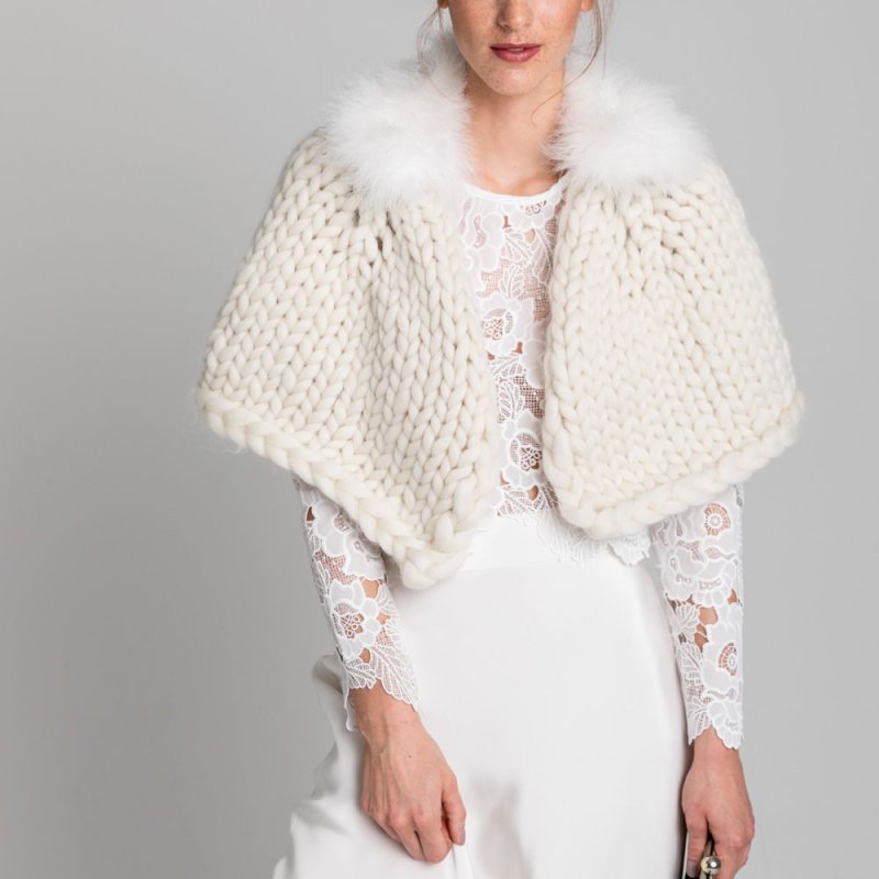 Nahaufnahme einer Frau in einem cremefarbenen, handgestrickten Braut-Cape mit Marabou-Kragen, kombiniert mit einem weißen Spitzen-Top und einem weißen Rock. Der Look eignet sich perfekt für eine elegante Hochzeit.