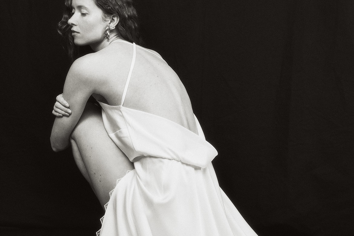 Ein schwarz-weiß Foto einer Braut, die ein rückenfreies Brautkleid trägt und sich mit dem Rücken zur Kamera wendet.