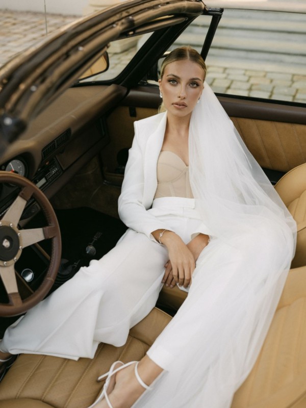 Eine Braut im Hochzeitsanzug mit Schleier, sitzend in einem klassischen Auto, in einer eleganten und modernen Pose.