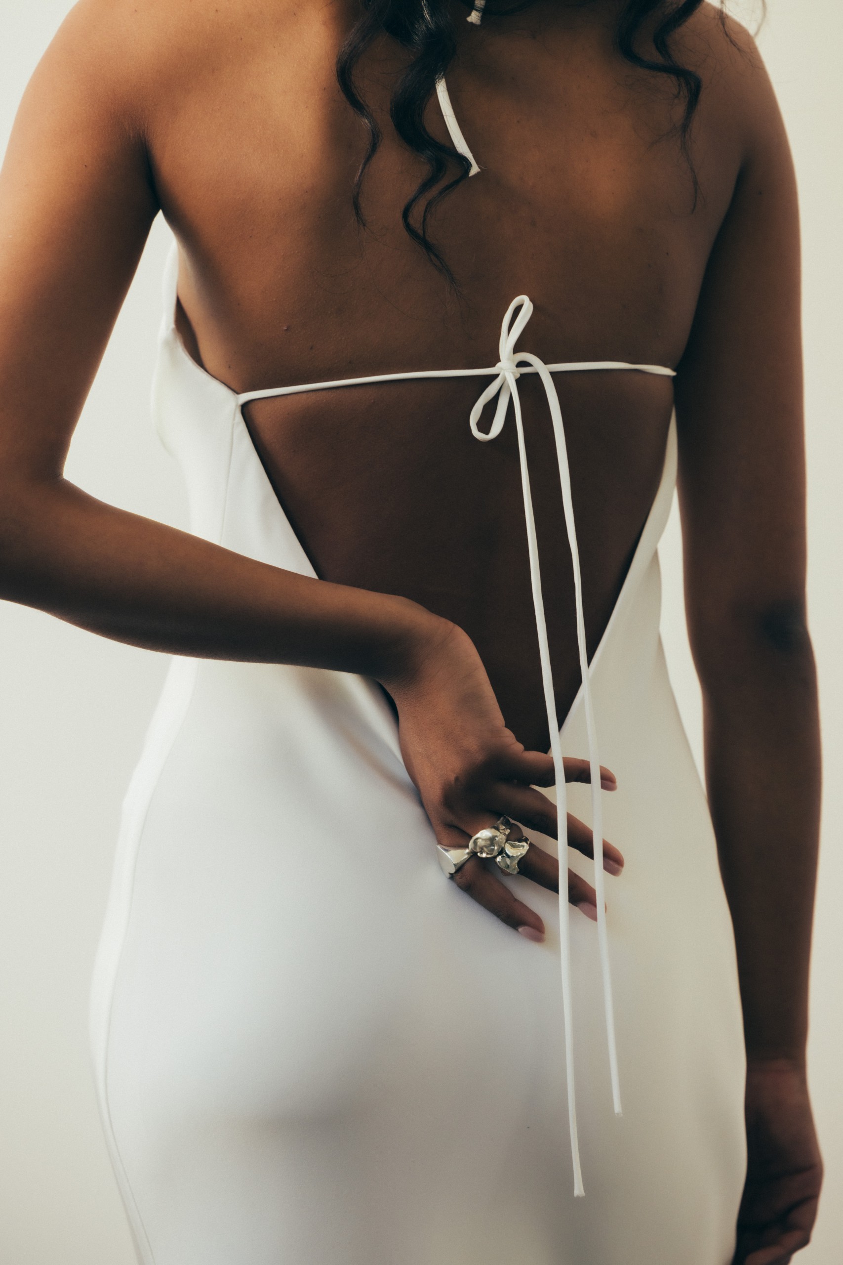 Rückenfreies, bodenlanges Brautkleid mit schmaler Silhouette und filigranen Trägern. Ein eleganter Look, der die Rückenpartie betont und perfekt für Sommerhochzeiten oder festliche Anlässe ist.