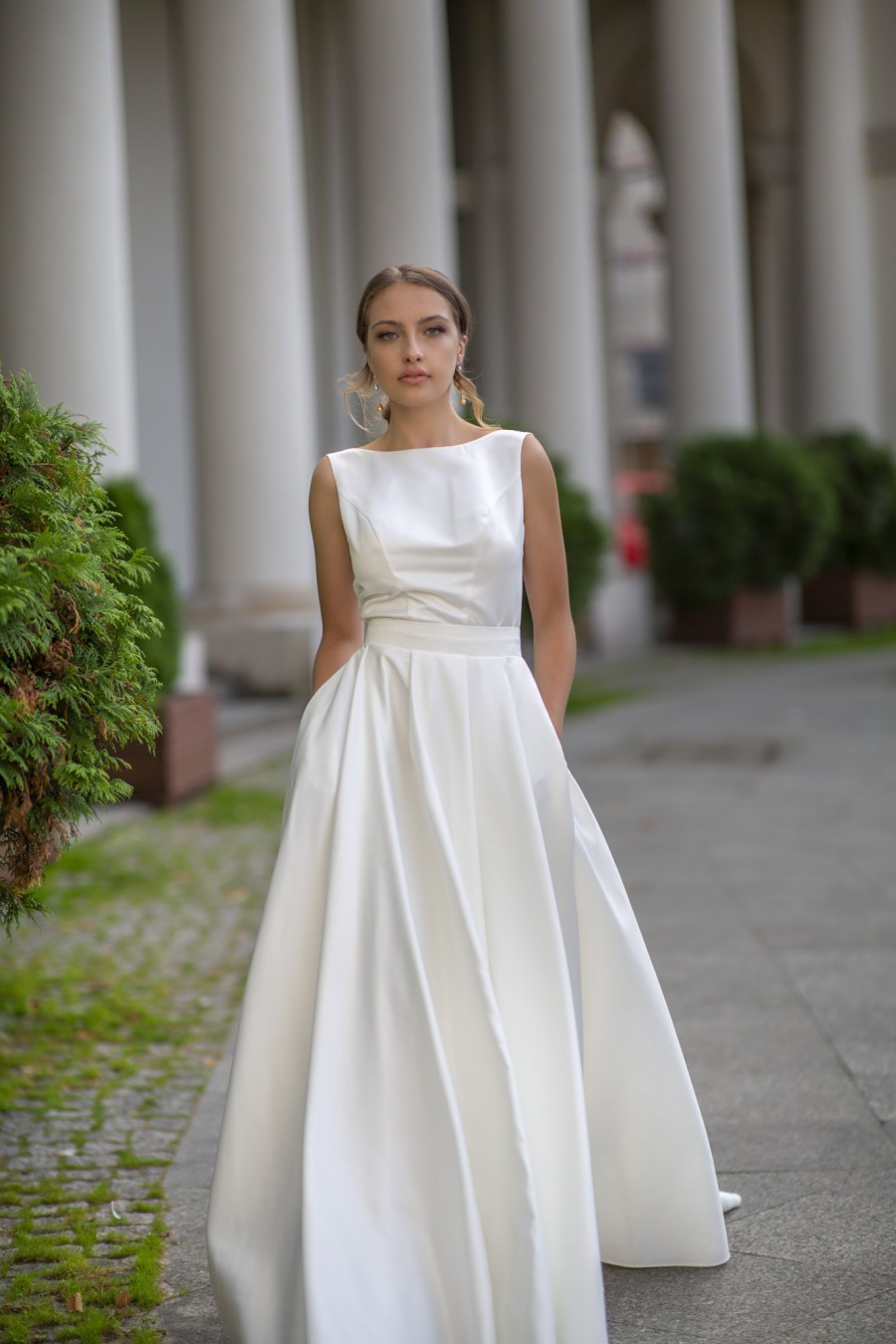 Elegantes Brautkleid mit hohem Rundhalsausschnitt und A-Linie-Rock, präsentiert vor einer historischen Säulenkulisse.