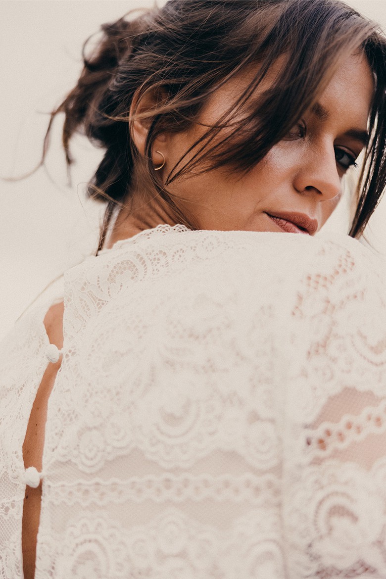 Eine Frau in einem Boho-Brautkleid, von unten fotografiert, blickt romantisch in die Kamera.