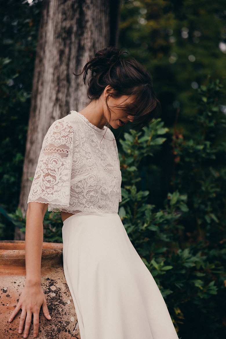 Eine Frau in einem boho Brautoutfit steht im Wald und schaut nach unten.